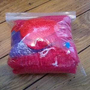May include: A clear plastic bag filled with red and purple netting. The netting is in a variety of shapes and sizes.
