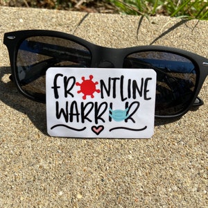 May include: Black sunglasses with a white sticker that reads "FRONTLINE WARRIOR" in black script. The sticker features a red coronavirus symbol, a blue face mask, and a pink heart.