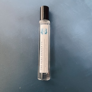 May include: A clear glass rollerball bottle with a black cap and a white label. The label reads "THE NERF HERDER CO. LUXURY GEEK CHIC ROLLERBALL COLOGNE BEN SOLO HERO EDITION BLACK PEPPER ATLAS CEDAR BEM SOLO"