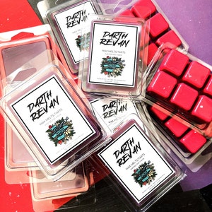 May include: A collection of purple and red wax melts in clear plastic packaging. The wax melts are labeled "Darth Revan" and feature a floral design. The wax melts are arranged on a purple and red surface.