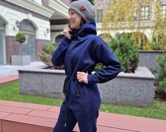 Set: jumpsuit en muts. Casual damesjumpsuit met capuchon, compleet met een grijze gebreide muts van natuurlijke wol.