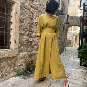 Pu&ograve; includere: Un lungo abito in lino giallo senape con bottoni sul davanti e una cintura. L'abito ha una vestibilit&agrave; rilassata e una gonna fluida.