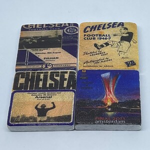 May include: Four vintage-style coasters featuring the Chelsea Football Club logo. The coasters are made of a light brown material with blue edges. The top coaster features a drawing of a player in a Chelsea uniform. The second coaster features a drawing of a player in a Chelsea uniform. The third coaster features a drawing of a player in a Chelsea uniform. The fourth coaster features a drawing of a player in a Chelsea uniform.