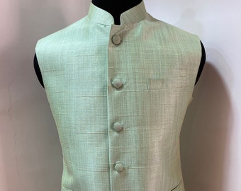 May include: A light green sleeveless vest with a mandarin collar and button closure. The vest has a textured fabric and two pockets.