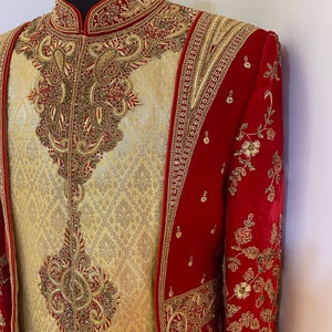 May include: A red and gold embroidered men's jacket with a matching gold and cream embroidered shirt. The jacket has a stand-up collar and long sleeves. The shirt has a mandarin collar and is tucked into the jacket.