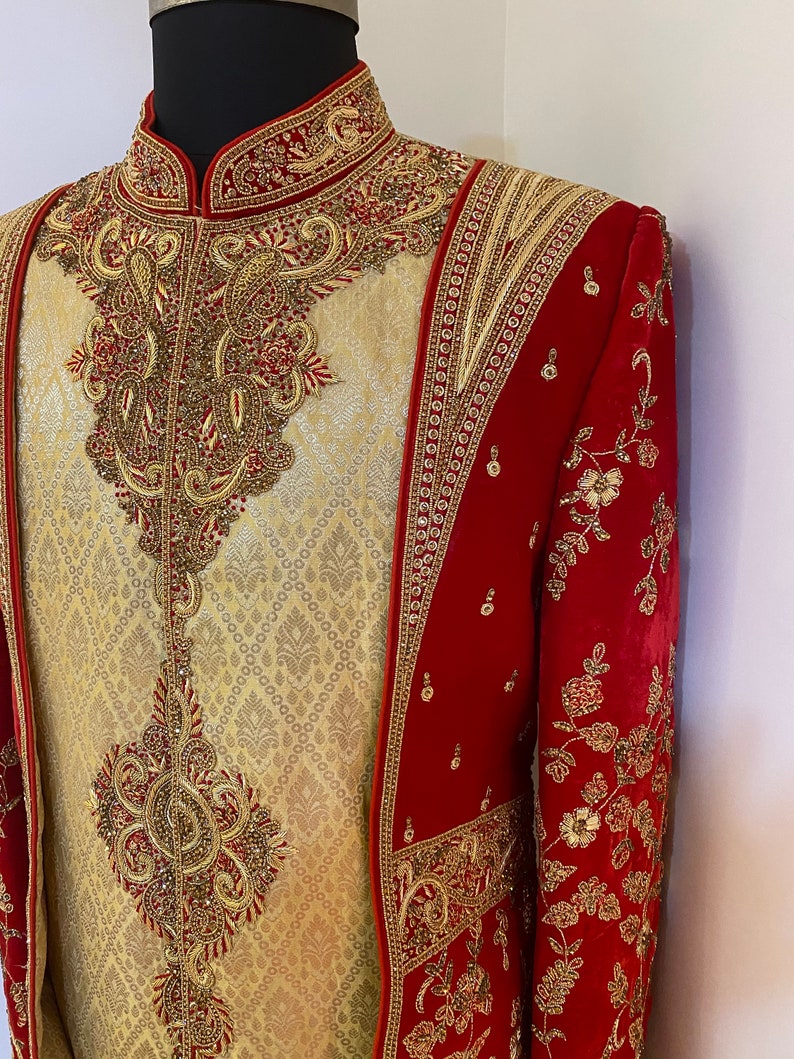 May include: A red and gold embroidered men's jacket with a matching gold and cream embroidered shirt. The jacket has a stand-up collar and long sleeves. The shirt has a mandarin collar and is tucked into the jacket.