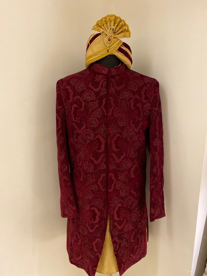 May include: A maroon velvet kurta with a floral pattern and a gold and maroon turban. The kurta has a long, flowing design and a stand-up collar.