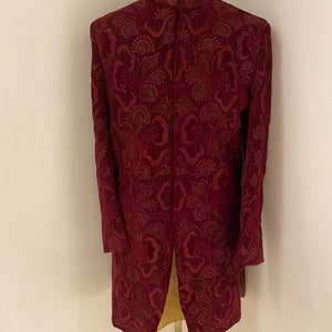 May include: A long, burgundy jacket with a mandarin collar and a floral pattern. The jacket is made of a soft, velvet-like fabric.