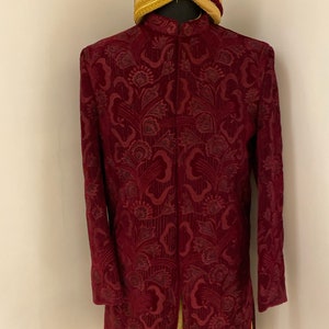 May include: A maroon velvet long-sleeved jacket with a floral pattern and a gold and maroon turban with a jewel on top.