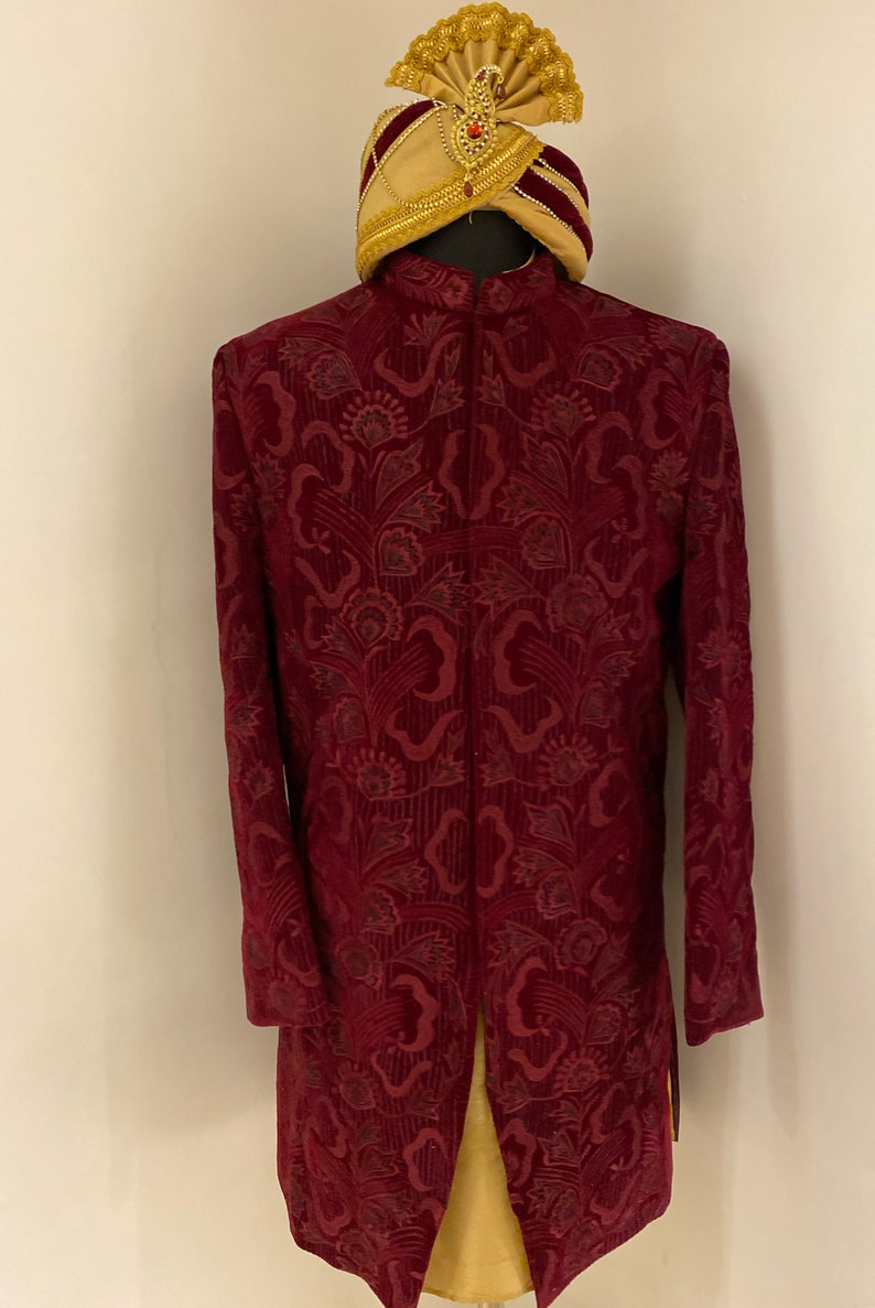 May include: A maroon velvet long-sleeved jacket with a floral pattern and a gold and maroon turban with a jewel on top.
