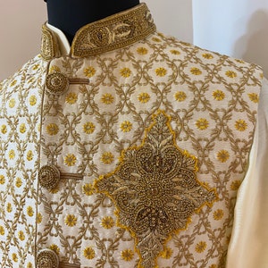 May include: A cream-coloured waistcoat with gold embroidery and a beaded design. The waistcoat has a mandarin collar and a button closure.
