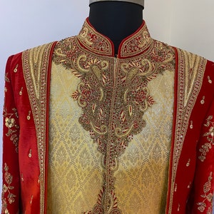 May include: A gold and red embroidered men's garment with a high collar and intricate detailing. The garment is made of a brocade fabric and features a paisley design.