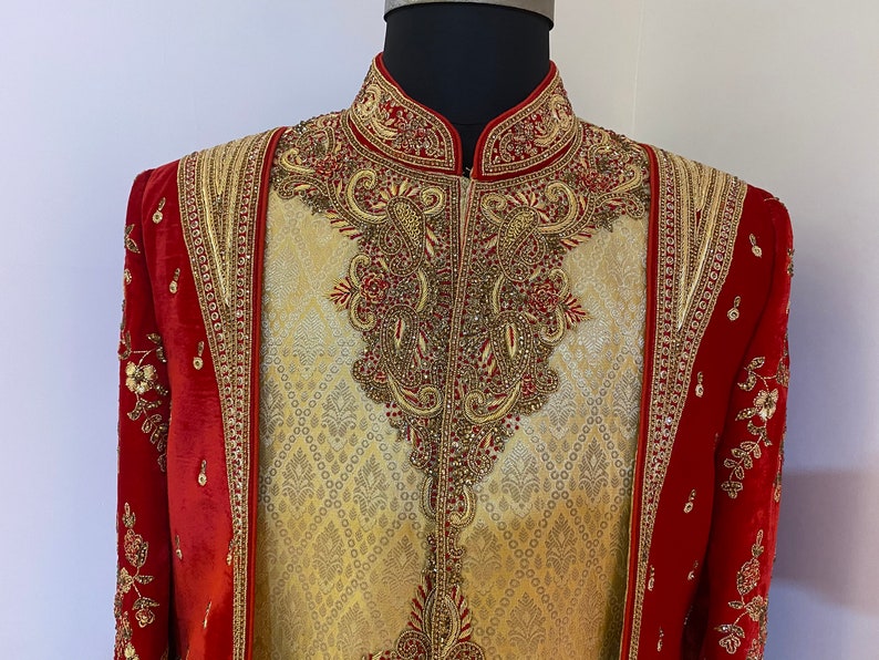 May include: A gold and red embroidered men's garment with a high collar and intricate detailing. The garment is made of a brocade fabric and features a paisley design.