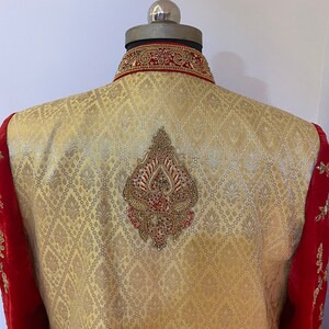 May include: A gold and red embroidered men's jacket with a diamond-shaped design on the back. The jacket has a high collar and a red velvet trim.
