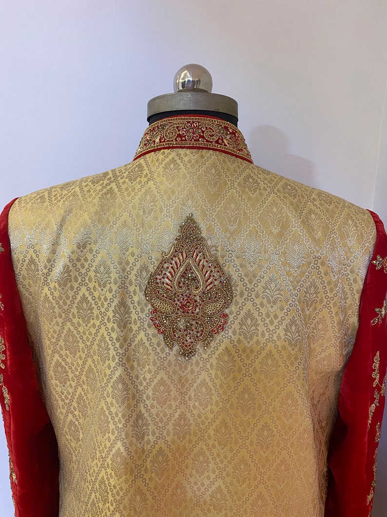 May include: A gold and red embroidered men's jacket with a diamond-shaped design on the back. The jacket has a high collar and a red velvet trim.