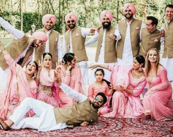 May include: A group of people wearing traditional Indian clothing, including pink and brown outfits, pose for a photo. The men are wearing turbans and waistcoats, while the women are wearing long dresses and jewellery. The group is smiling and laughing, creating a festive atmosphere.