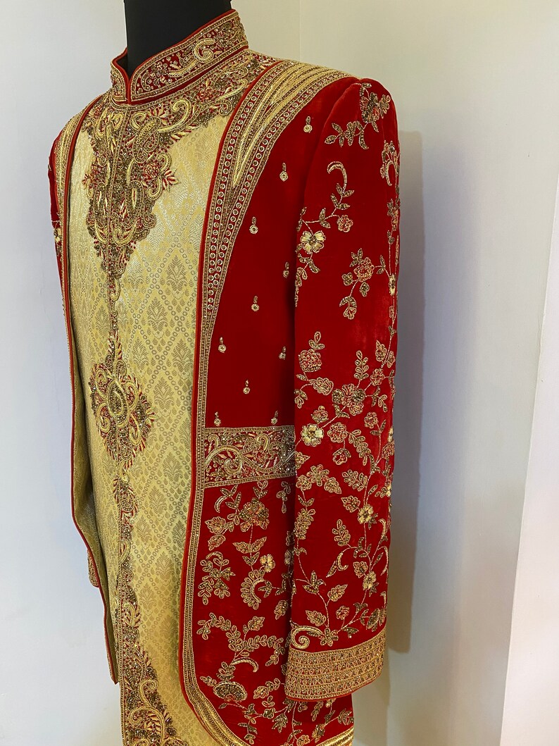 May include: A red and gold embroidered men's garment with a long, flowing design. The garment is made of a velvet fabric and features intricate floral patterns.