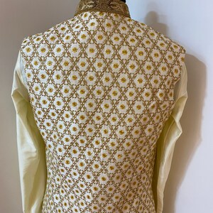 May include: A white waistcoat with a gold embroidered pattern. The pattern features a repeating design of small flowers and leaves.