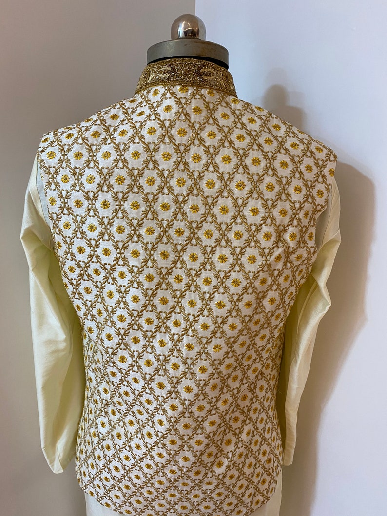 May include: A white waistcoat with a gold embroidered pattern. The pattern features a repeating design of small flowers and leaves.