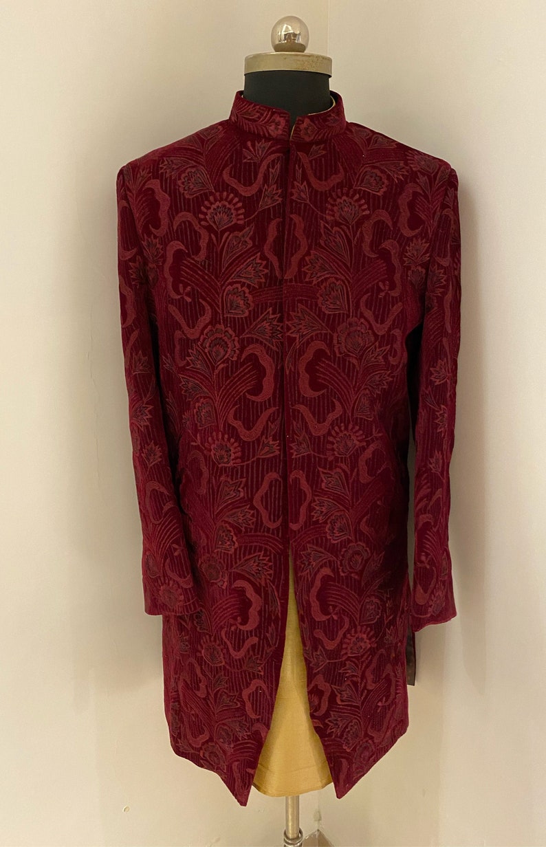 May include: A maroon velvet long-sleeved jacket with a floral pattern. The jacket has a mandarin collar and a front closure.