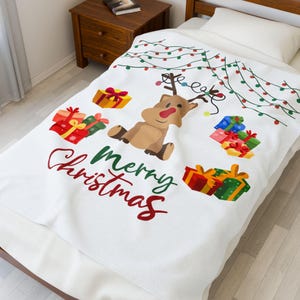 May include: White Christmas blanket with a cartoon reindeer, red-nosed and antlered, surrounded by colorful gift boxes and fairy lights. The words "merry Christmas" are written in red and green.