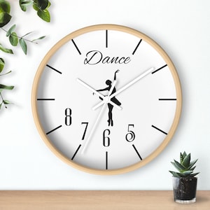 May include: A round wall clock with a light wood frame. The white clock face features black numerals, hands, and the word "Dance" above a ballerina silhouette. The clock is approximately 12 inches in diameter.