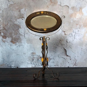 May include: An antique vanity mirror with an oval-shaped frame and a decorative stand. The frame is dark brown with gold floral accents. The stand has a curved design with gold floral details and a three-legged base.