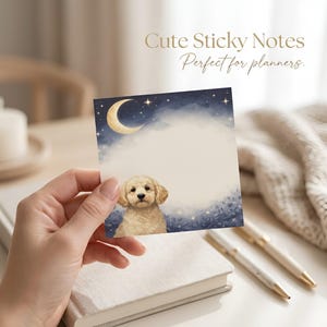 May include: Square sticky note with a watercolor illustration of a puppy, moon, and stars. The text "Cute Sticky Notes" and "Perfect for planners" is printed at the top. The note is held in front of a book and pens.