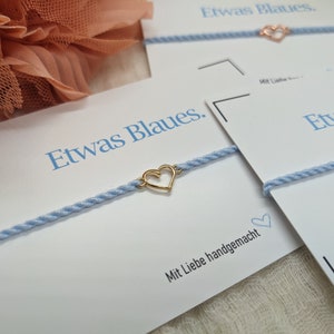 May include: A light blue bracelet with a gold heart charm. The bracelet is on a white card with the text "Etwas Blaues." and "Mit Liebe handgemacht".