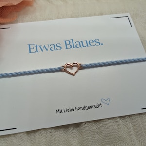 May include: A light blue bracelet with a rose gold heart charm. The bracelet is on a white card with the text "Etwas Blaues." and "Mit Liebe handgemacht".
