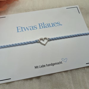 May include: A light blue bracelet with a silver heart charm. The bracelet is on a white card with the text "Etwas Blaues." and "Mit Liebe handgemacht".