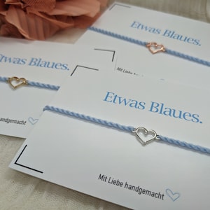May include: Three cards with the text "Etwas Blaues." and the phrase "Mit Liebe handgemacht" on each card. Each card has a blue string bracelet with a heart charm.
