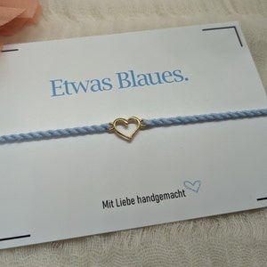 May include: A light blue bracelet with a gold heart charm. The bracelet is on a white card with the text "Etwas Blaues." and "Mit Liebe handgemacht".
