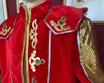 May include: A red velvet jacket with gold and silver trim. The jacket has a high collar and a decorative design on the front. The sleeves are decorated with gold sequins.