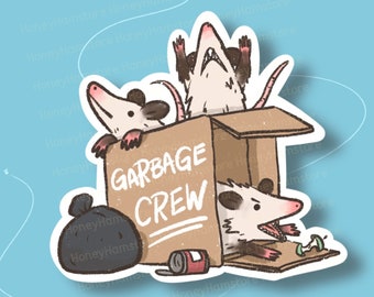 May include: A sticker featuring three cartoon opossums in a cardboard box with the words "Garbage Crew" written on the side. The opossums are brown and white with black eyes and noses. The box is brown with a white label. There is a black garbage bag and a can in the bottom of the box.