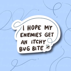 May include: A white sticker with the text "I HOPE MY ENEMIES GET AN ITCHY BUG BITE" in black, outlined by a light blue speech bubble. A small cartoon bee is on the bottom right. The background is light blue with drawn lines.