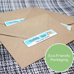 May include: Kraft paper envelopes with "Thank You" stickers. The stickers have a light blue background with the text "Thank You" and "Your order is here!" in a playful font. The image also includes a green circle with the text "Eco-Friendly Packaging".