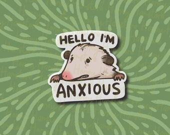 Op de afbeelding: Een sticker met een cartoon-opossum met een bezorgde uitdrukking. De sticker zegt "Hello I'm Anxious" in een witte spraakballon.