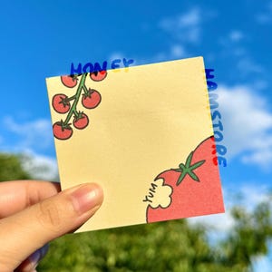 May include: A square, light yellow sticky note with a red tomato illustration and the word "Yum". The note also features a branch of red tomatoes and the words "HONEY" and "HAMSTORE" in blue.