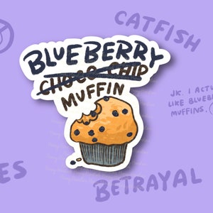 May include: A sticker featuring a cartoon blueberry muffin with a bite taken out. The text on the sticker reads "Blueberry Muffin" with "Choc Chip" crossed out. Other words include "Catfish", "Lies", "Betrayal", and "JK. I actually like blueberry muffins."