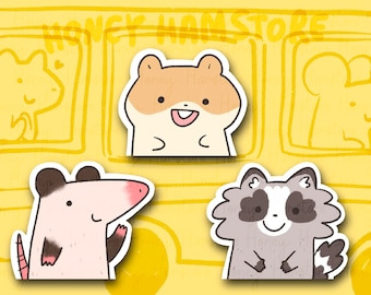 May include: Cute sticker set featuring a hamster, opossum, and raccoon. The hamster is light brown and white, the opossum is light gray with a pink nose, and the raccoon is gray and white. The background is yellow with the text "HONEY HAM STORE".