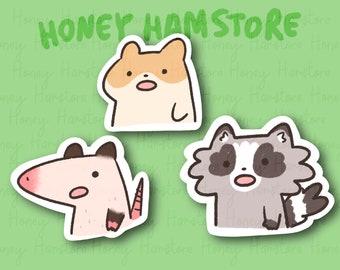 May include: Three cute animal stickers: a hamster, a raccoon, and an opossum. The hamster is tan and white, the raccoon is gray and white, and the opossum is pink and white. The stickers are on a green background with the text "HONEY HAMSTORE".