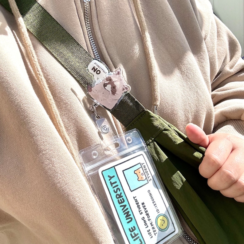 May include: A green and brown lanyard with a clear plastic ID holder. The ID holder contains a blue and white card that reads "Life University" and "Life Long Student Forever." A small raccoon charm is attached to the lanyard.