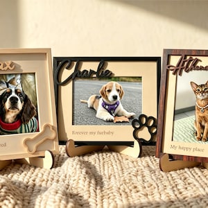 May include: Three rectangular wooden picture frames with custom names and pet-themed cutouts. The first frame is light wood with 'Max' and 'Loved' text and a bone shape. The second is black with 'Charlie' and 'Forever my furbaby' text and a paw print. The third is dark wood with 'Athena' and 'My happy place' text and a fish shape.