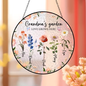 May include: A round, pink and white stained glass suncatcher with the text "Grandma's garden LOVE GROWS HERE" and the names Alex, David, Noah, Mary, and Lisa. The suncatcher features a variety of flowers and butterflies.
