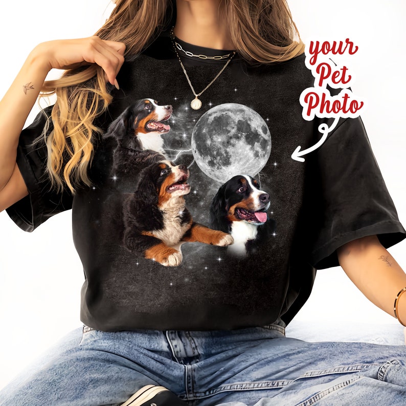 May include: Black t-shirt with a design of three Bernese Mountain Dogs looking up at a full moon with stars in the background. The text "your Pet Photo" is written on the shirt.