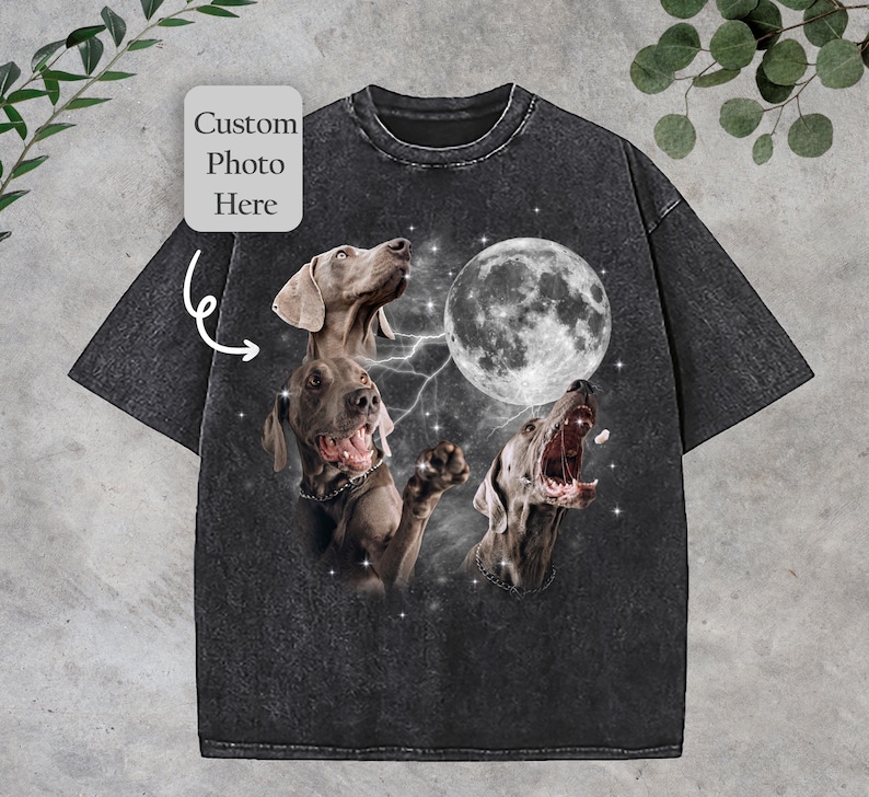 May include: A black t-shirt with a vintage look featuring three Weimaraner dogs howling at the moon. The moon is full and white, and the dogs are silhouetted against a starry sky. The shirt has a distressed look and feel.