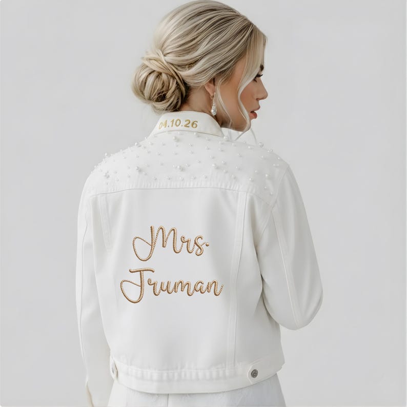 May include: A white denim jacket featuring gold embroidered text that reads Mrs. Truman on the back and 04.10.26 on the collar. The upper back and shoulder area are embellished with scattered white pearls of varying sizes across the fabric.