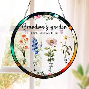 May include: A round stained glass window hanging with a green, orange, and brown frame. The window features a floral design with four different flowers and the text "Grandma's garden LOVE GROWS HERE". The names Alex, David, Mary, and Lisa are written below the flowers.