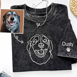 May include: A black t-shirt with a white line drawing of a dog's face on the front. The dog's name, "Dusty", is embroidered on the sleeve with a paw print.